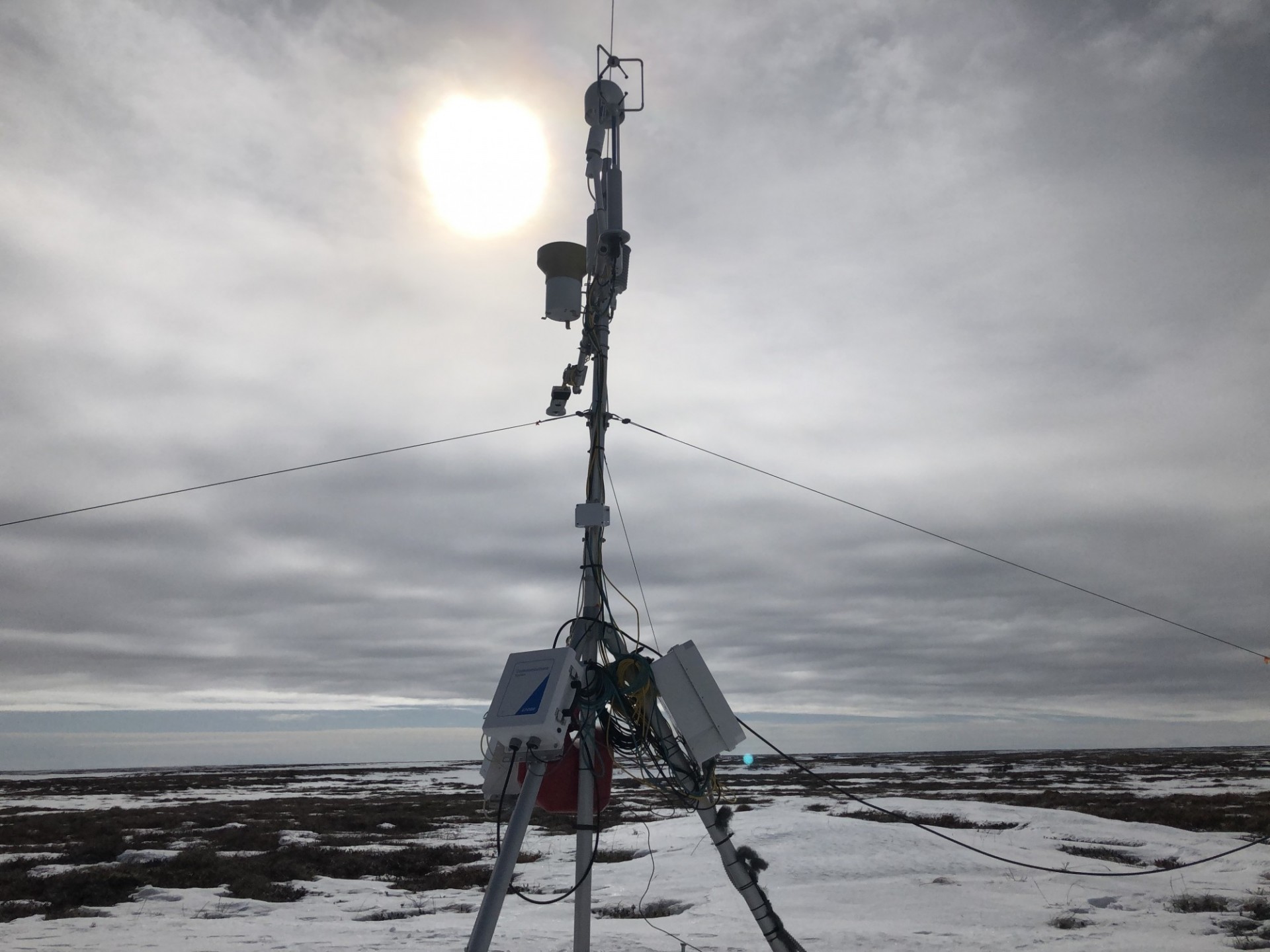 photo of eddy covariance flux tower in snowy landscape, sun through clouds in background